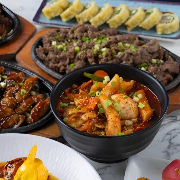 Ohya Sushi's Korean dishes: bulgogi, tteokbokki, and fried sushi rolls on a marble table.
