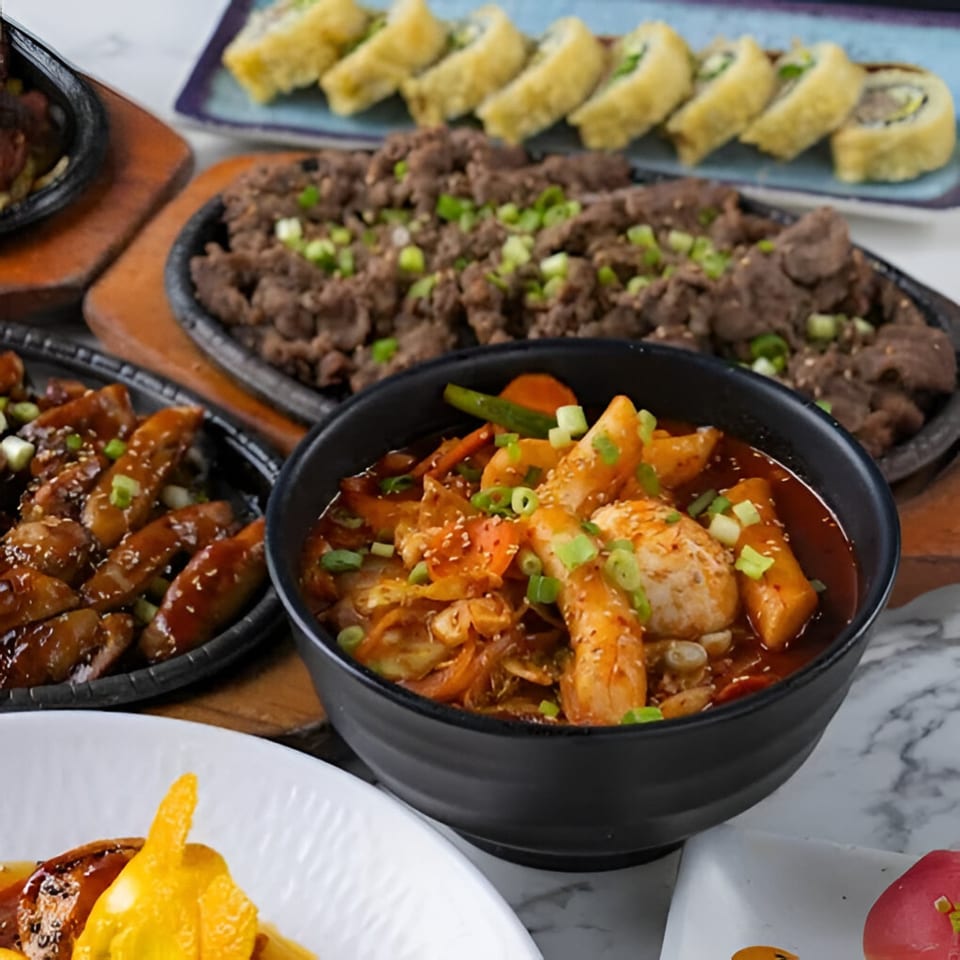 Ohya Sushi's Korean dishes: bulgogi, tteokbokki, and fried sushi rolls on a marble table.